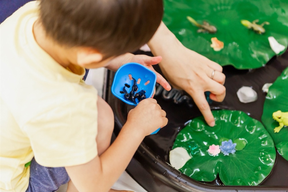 子どもが小さな器に、トレイの中のものをすくい入れている